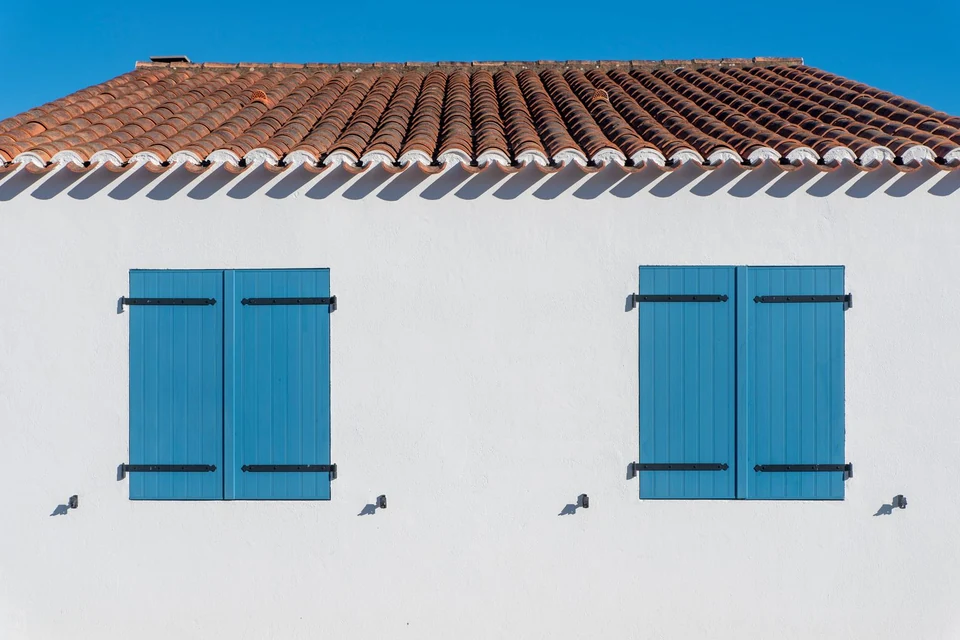 Façade blanche aux volets bleus sous un toit de tuiles
