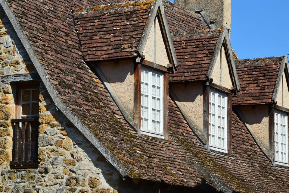 Toit ancien en tuiles moussues percé de lucarnes, sur une maison en pierre