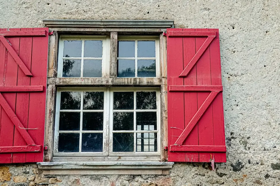 Volets en bois rouges autour d'une fenêtre ancienne sur un mur enduit